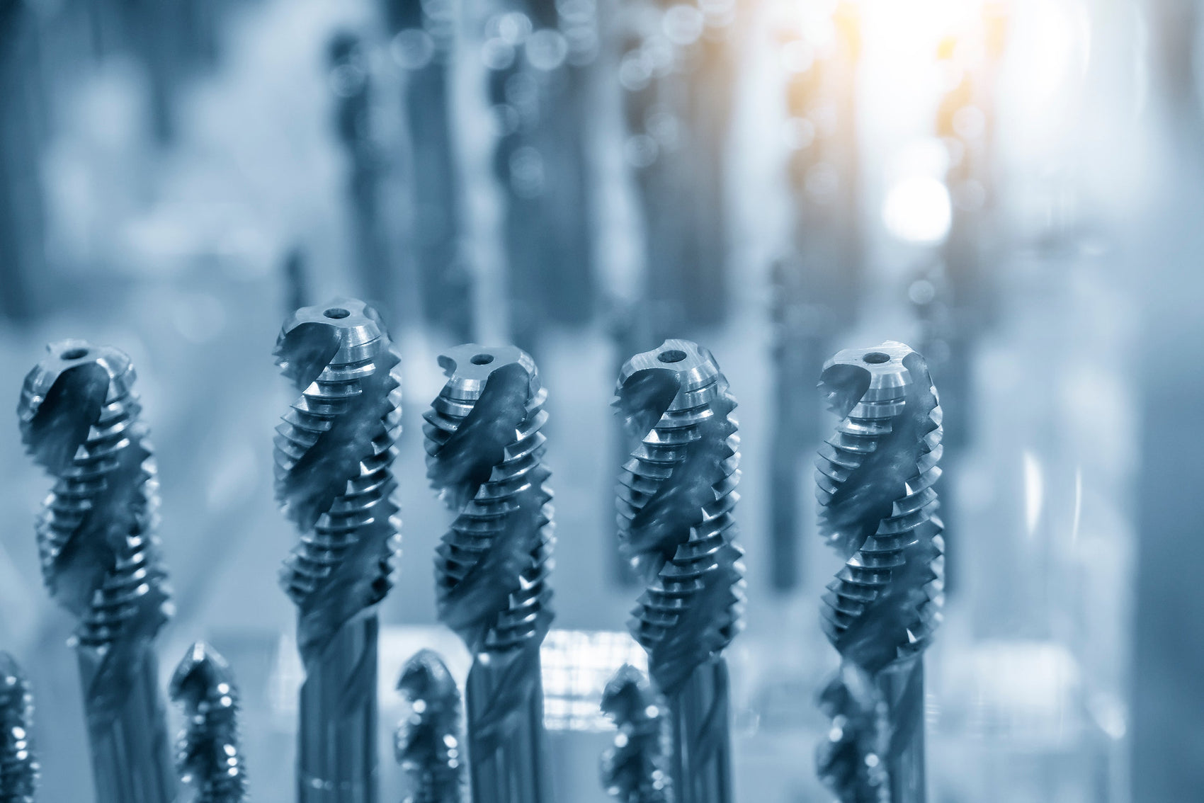 Close-up image of multiple metal cutting tools, specifically end mills, arranged vertically in a storage rack.